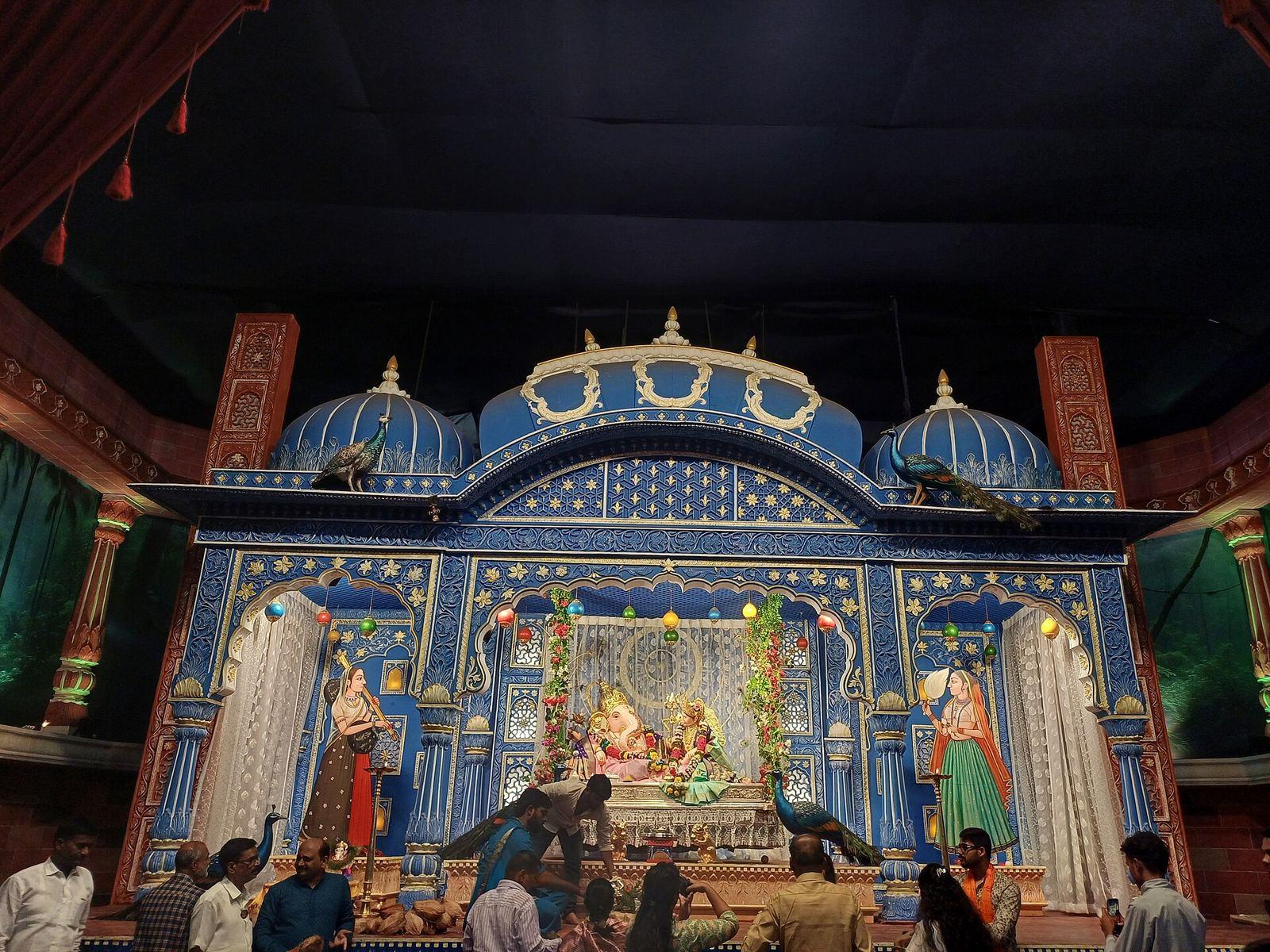 Festival idol of Akhil Mandai Mandal Ganpati, crowned and seated in a blue and gold mandap